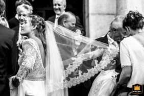 A boy playfully tugs at a bride's veil in Thorens, France. The black and white wedding photo shows the child interacting with the bridal accessory.